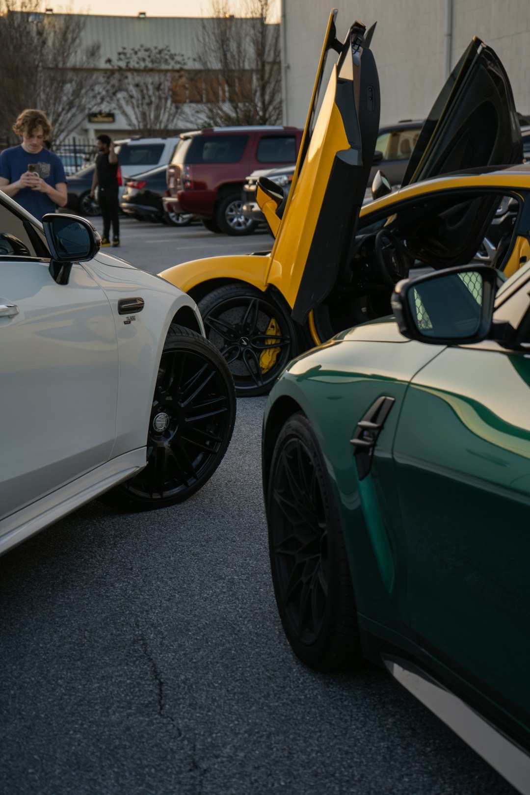 Three luxury cars parked outside, yellow sports car doors open.